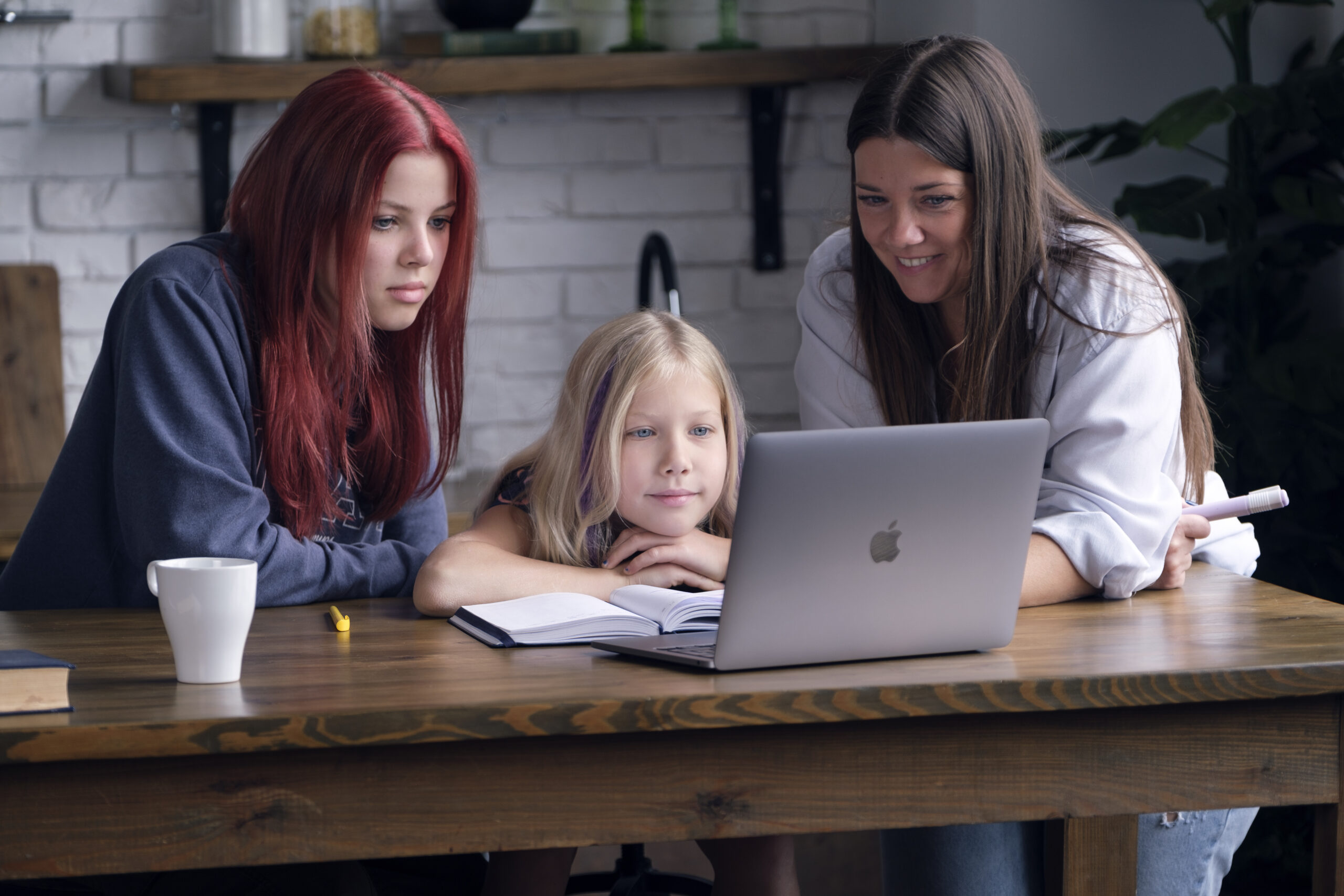 Мама і дочки за столом, займаються онлайн-навчанням, дивлячись на ноутбук.